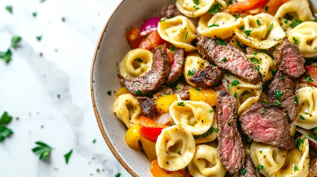 A comforting bowl of cheesesteak tortellini with bell peppers and onions.