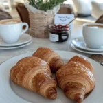 A breakfast table set with coffee, croissants, and jam for a classic French breakfast.